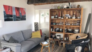 Een gezellige woonkamer met een grijze bank, een houten boekenkast vol glaswerk en een vloerkleed met een patroon.