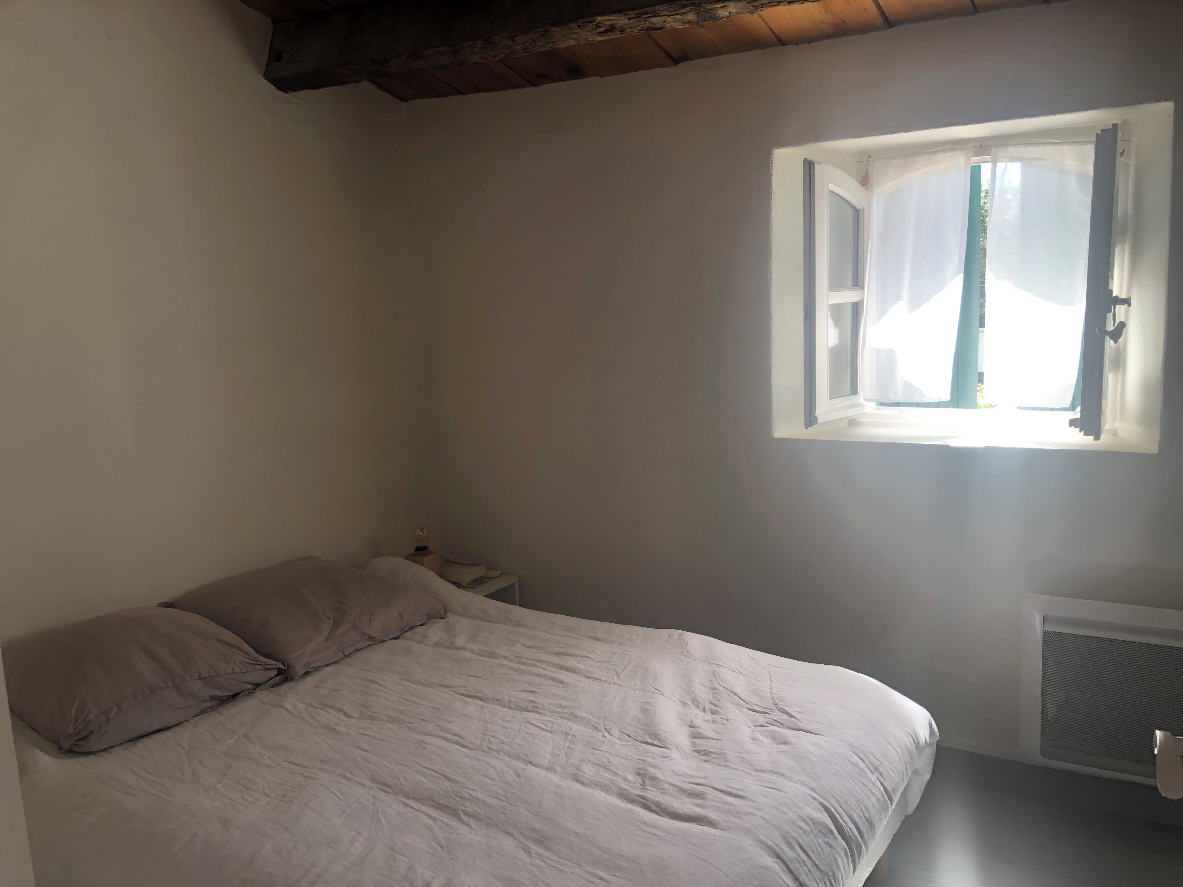 Une chambre avec un lit simple, une table de chevet, une fenêtre avec des rideaux et un radiateur.