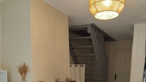 Una sala de estar con sofá, lámpara colgante, escalera y puerta.