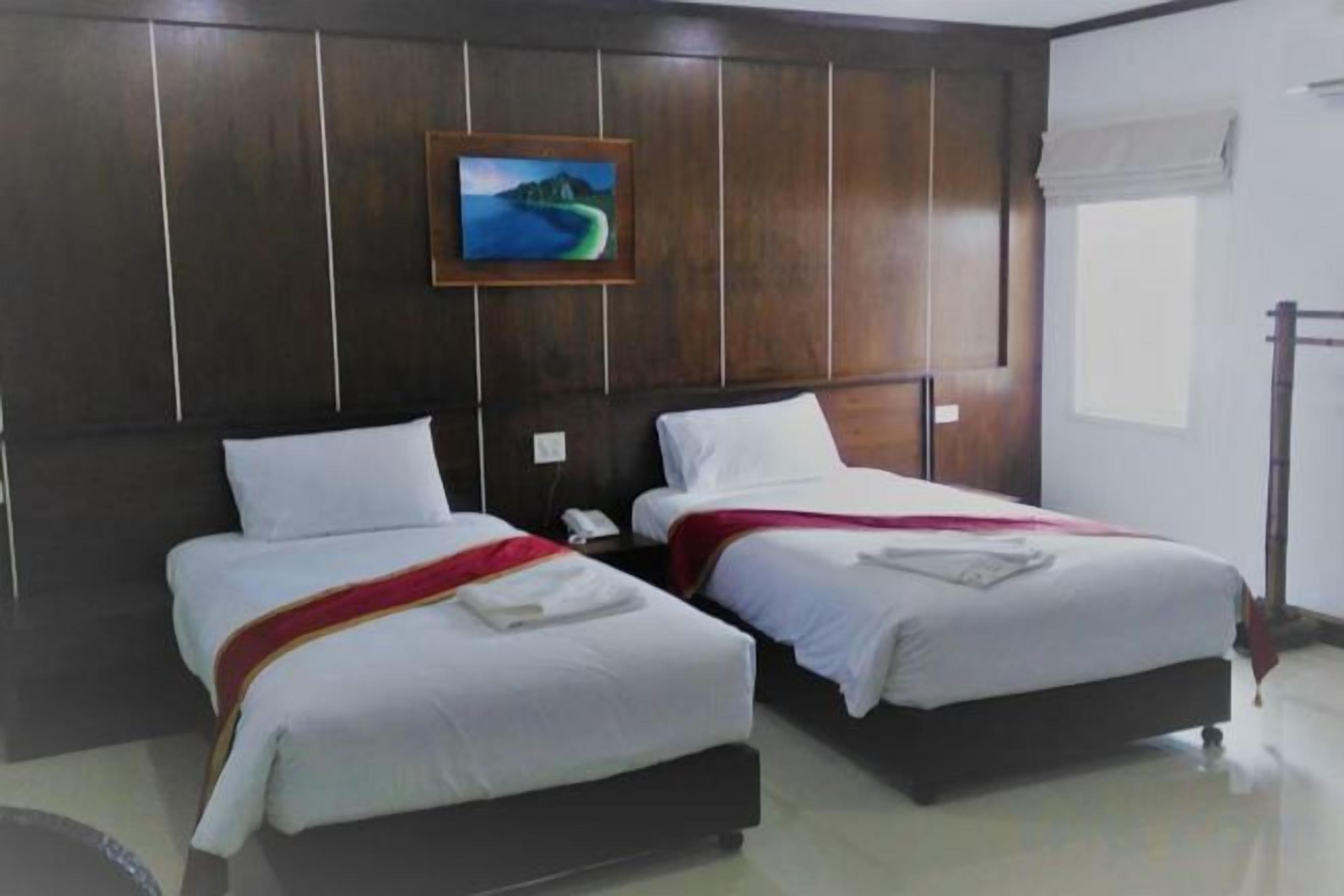 Quarto de hotel com duas camas, um quadro na parede e uma janela com cortina.