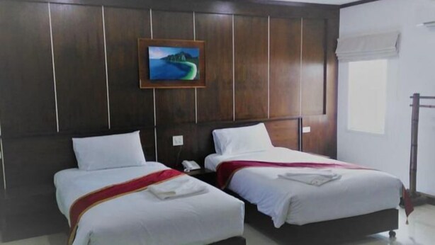 Une chambre d’hôtel avec deux lits, un tableau au mur et une fenêtre avec un rideau.