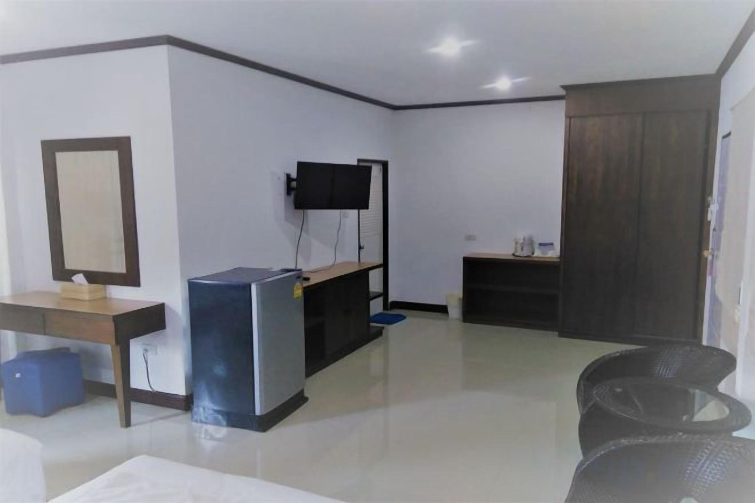 Quarto com televisão de tela plana na parede, escrivaninha com cadeira, pequena geladeira e sofá.