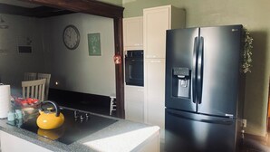 Una cucina con frigorifero nero, dispenser d'acqua, orologio e bollitore sul piano di lavoro.