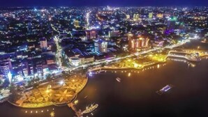 An aerial view of a cityscape at night with illuminated buildings, a waterfront promenade, and boats on the water. - Amaris Hotel Pettarani - Makassar (Panakkukang)