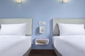 Una habitación de hotel con dos camas, una mesita de noche con teléfono y una lámpara de pared.