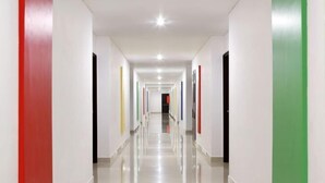 A long, well-lit hallway with white walls and doors in various colors. - Amaris Hotel Pettarani - Makassar (Panakkukang)
