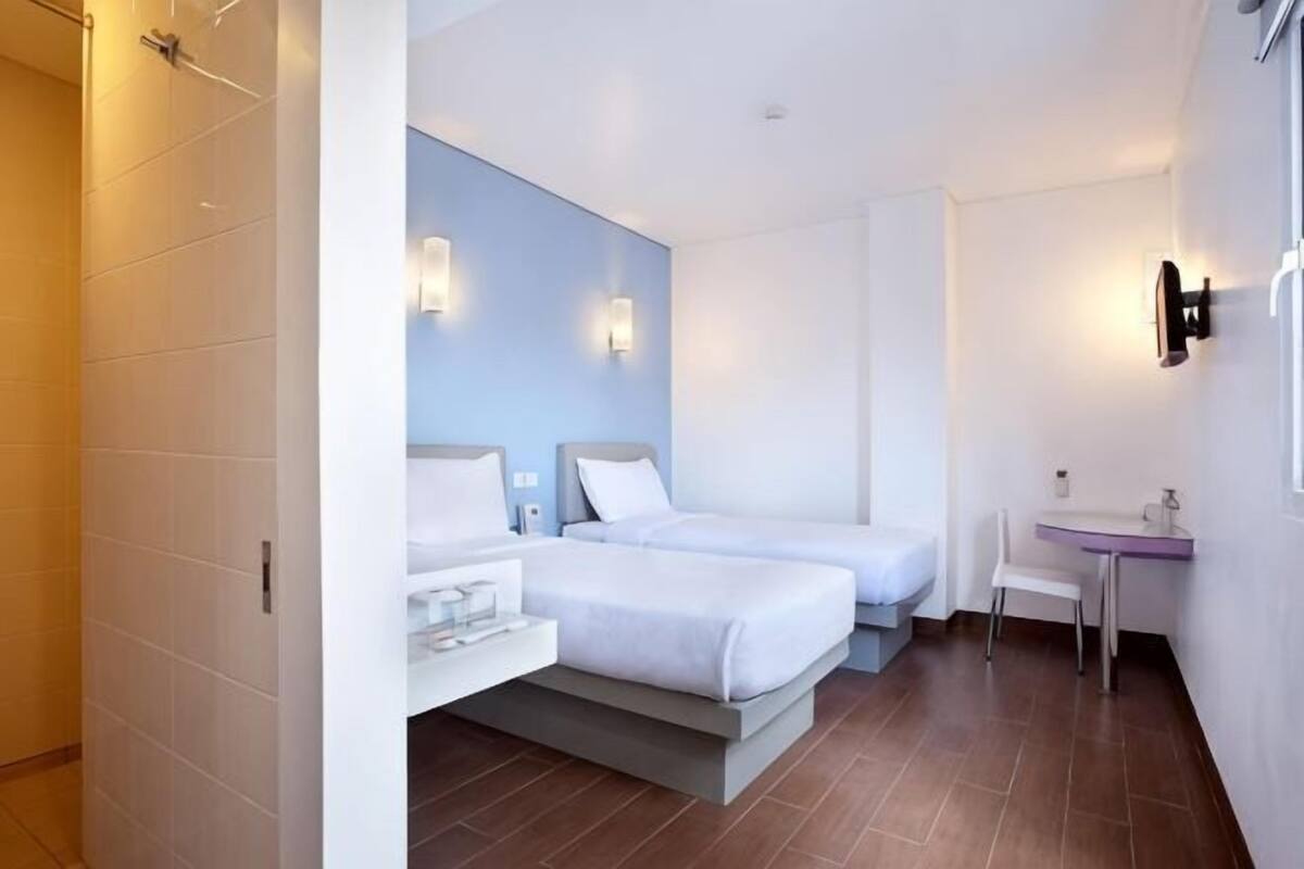 Une chambre d’hôtel avec deux lits, un petit bureau, une chaise et une salle de bain équipée d’un lavabo et d’un miroir.