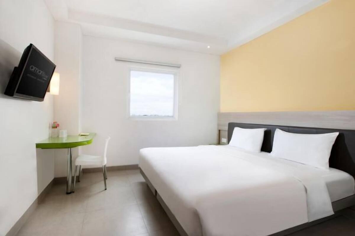 Une chambre d’hôtel avec un lit, un bureau, une chaise, une télévision et une fenêtre.