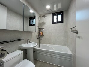 A modern bathroom with a white sink, toilet, and bathtub. There is a mirror above the sink, and a showerhead above the bathtub. - Sea & You pool villa pension (Taean)