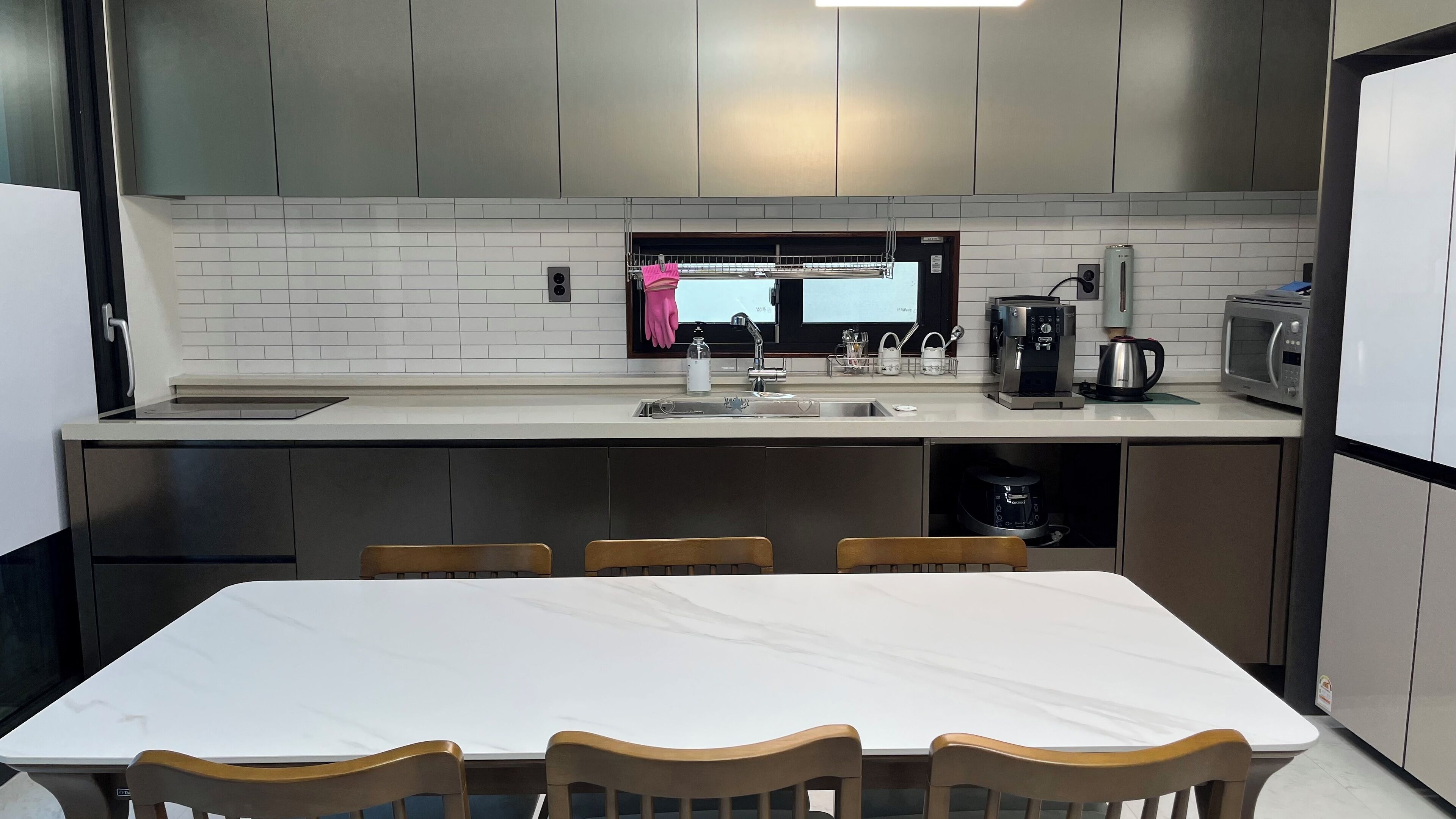 A modern kitchen with a white countertop, stainless steel appliances, and a dining area with a white table and wooden chairs.