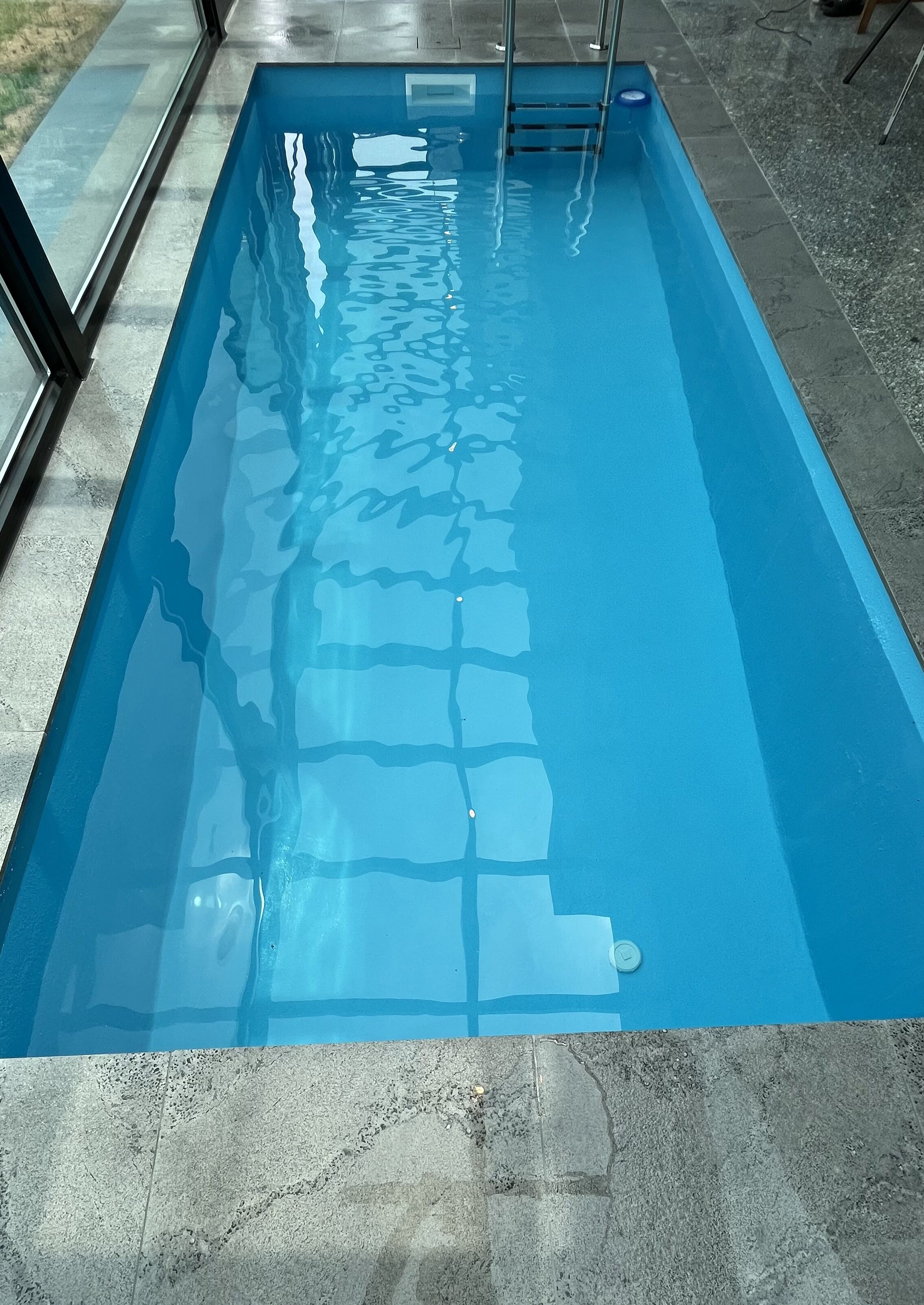 Una piscina rectangular con agua azul cristalina, rodeada por un solárium empinado.