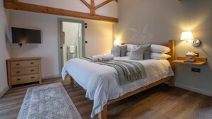 A bedroom with a wooden ceiling, a bed with white bedding, a nightstand with a lamp, a TV on the wall, and a small wooden dresser. - Luxury farm cottage in the beautiful Peak District (Eyam)