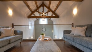 A loft-style room with wooden beams, two grey sofas, a wooden coffee table, and a small plant. - Luxury farm cottage in the beautiful Peak District (Eyam)