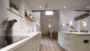 A modern kitchen with white cabinets, a black stove, and wooden flooring. - Luxury farm cottage in the beautiful Peak District (Eyam)