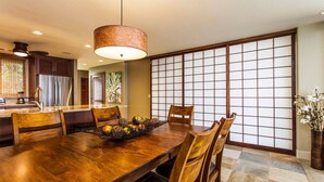 A traditional Japanese-style dining room with a wooden table, chairs, and a decorative fruit basket. - Exquisite Oceanfront Beautifully Upgraded Corner Unit - Vrkcv (Kailua-Kona)