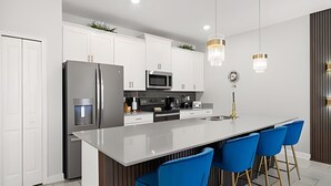 A modern kitchen with white cabinets, stainless steel appliances, and a central island with blue bar stools. - 4BR w/ Mickey & Mario Rooms + Heated Pool (Davenport)