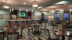 A hotel dining area with multiple tables and chairs, a bar, and a television screen displaying a program. - 4BR w/ Mickey & Mario Rooms + Heated Pool (Davenport)