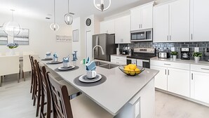 Una cucina moderna con mobili bianchi, un'isola centrale e lampade dal design contemporaneo.