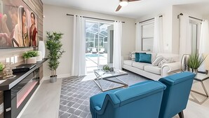 Un soggiorno moderno con un divano bianco, poltrone blu, un tavolino da caffè in vetro e una ventola a soffitto.