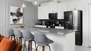 Una cocina moderna con una isla central, electrodomésticos de acero inoxidable y taburetes grises.