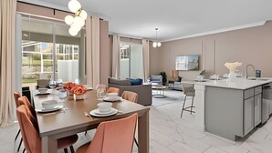 Une cuisine moderne dotée d’un îlot central, d’un coin repas avec une table pour quatre personnes et d’un espace salon avec un canapé et des fauteuils.