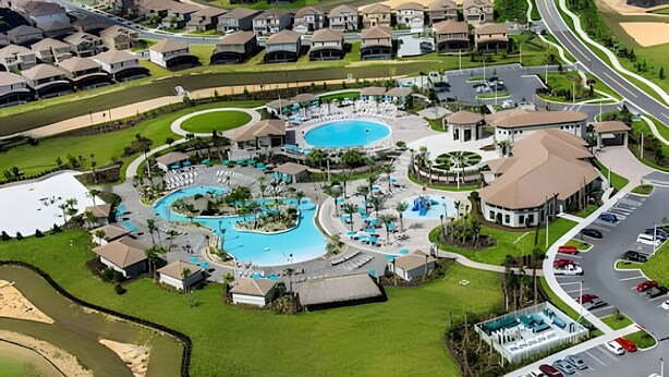 Oversigtsbillede af et boligområde med flere huse, en stor swimmingpool og en parkeringsplads.