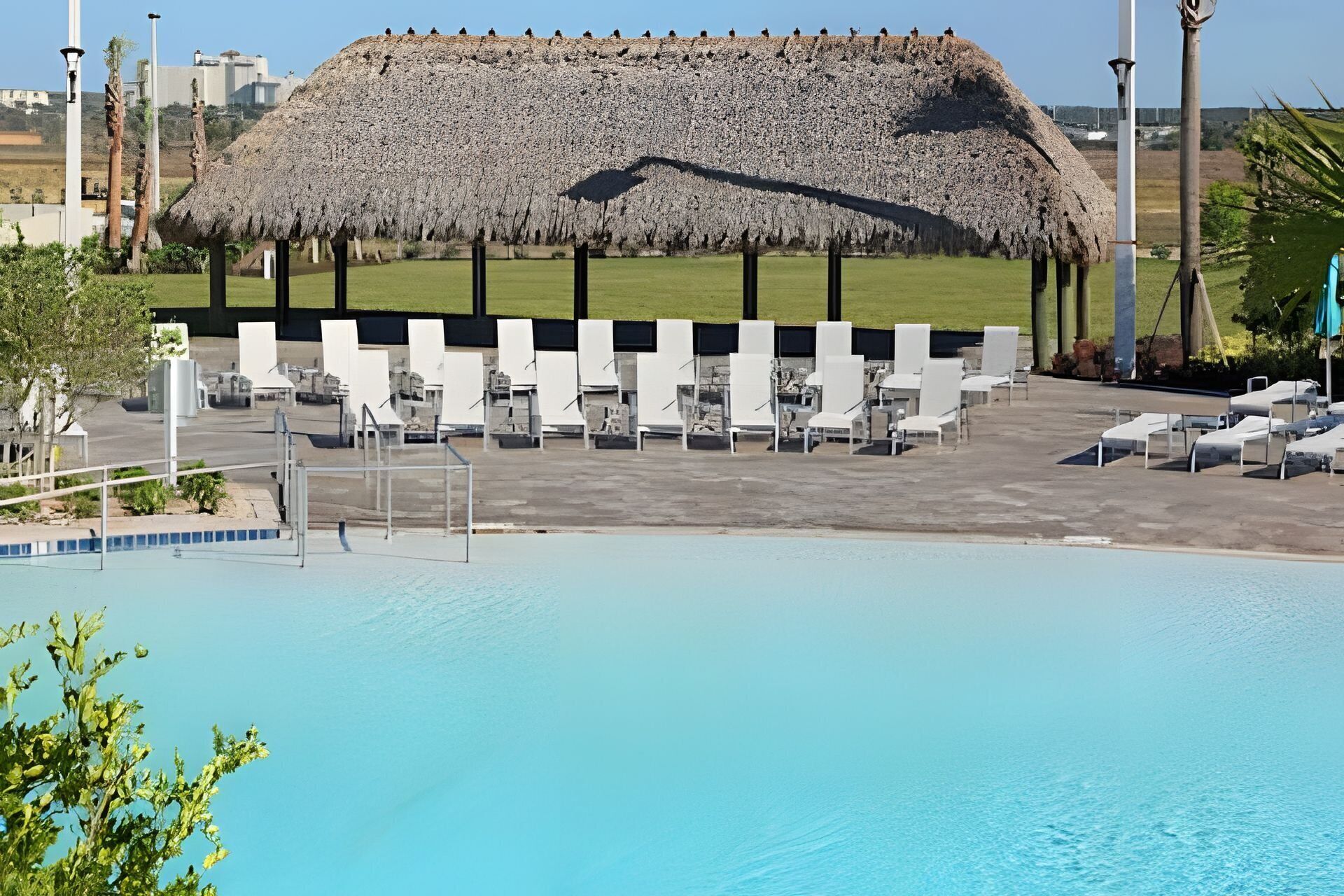Un'area piscina con poltrone da relax bianche e una struttura con tetto di paglia.