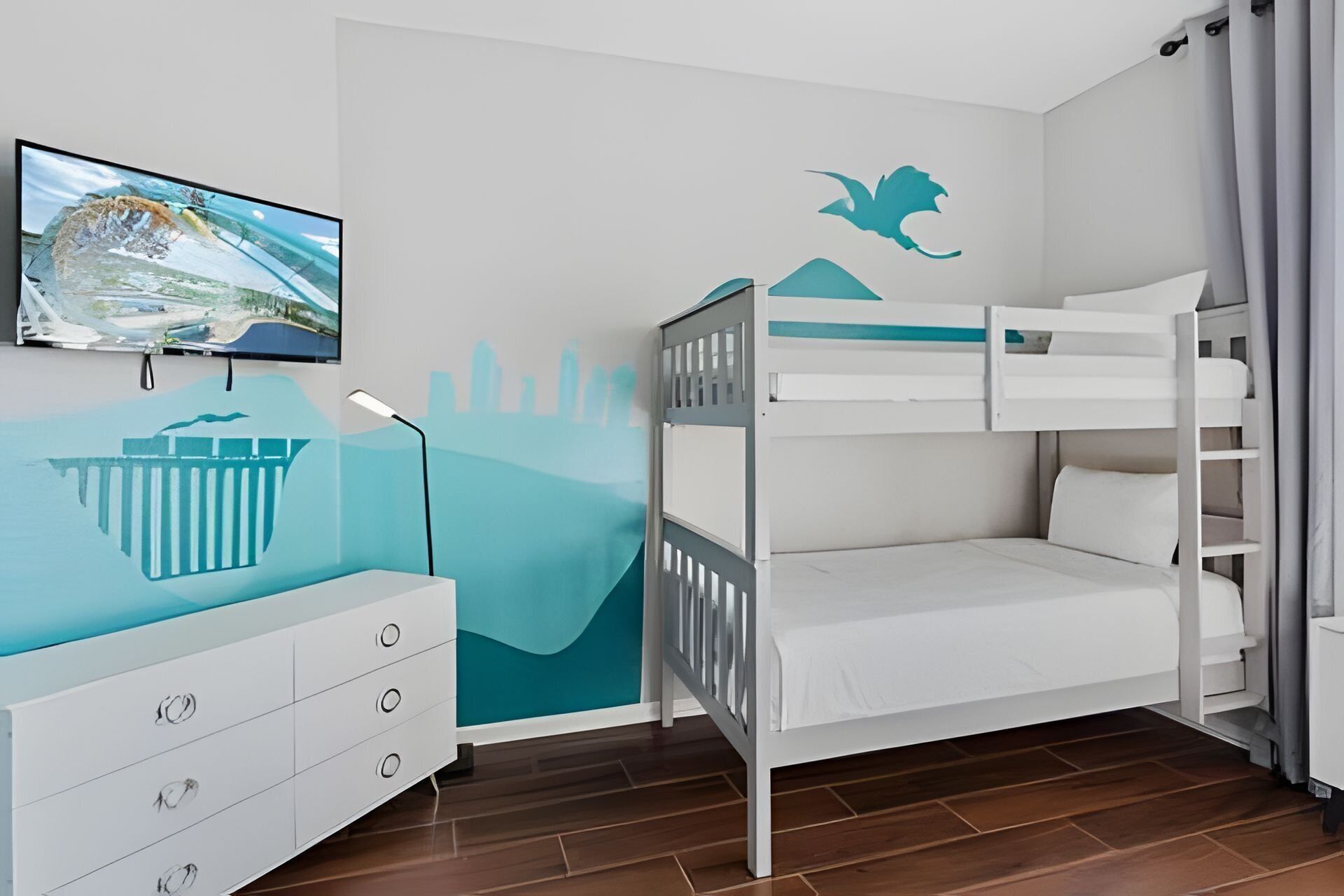 Habitación infantil con literas, cómoda, televisor y un mural en la pared.