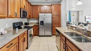 A modern kitchen with wooden cabinets, stainless steel appliances, granite countertops, and a built-in sink. - Vista Cay 4BR Condo w/ Balcony & Foosball Fun (Orlando)