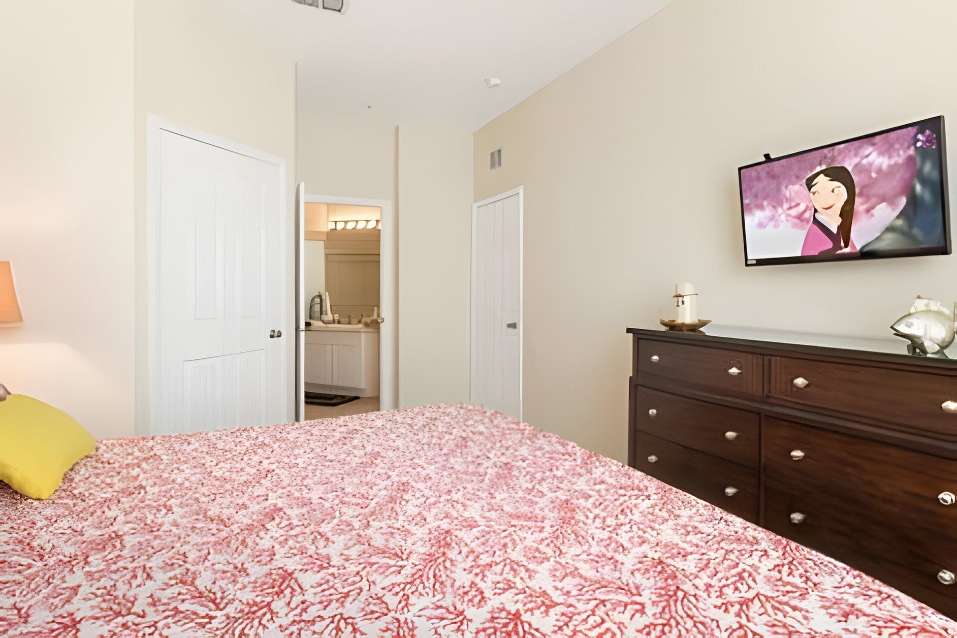 A bedroom with a bed, a dresser, a TV, and a bathroom visible through an open door.
