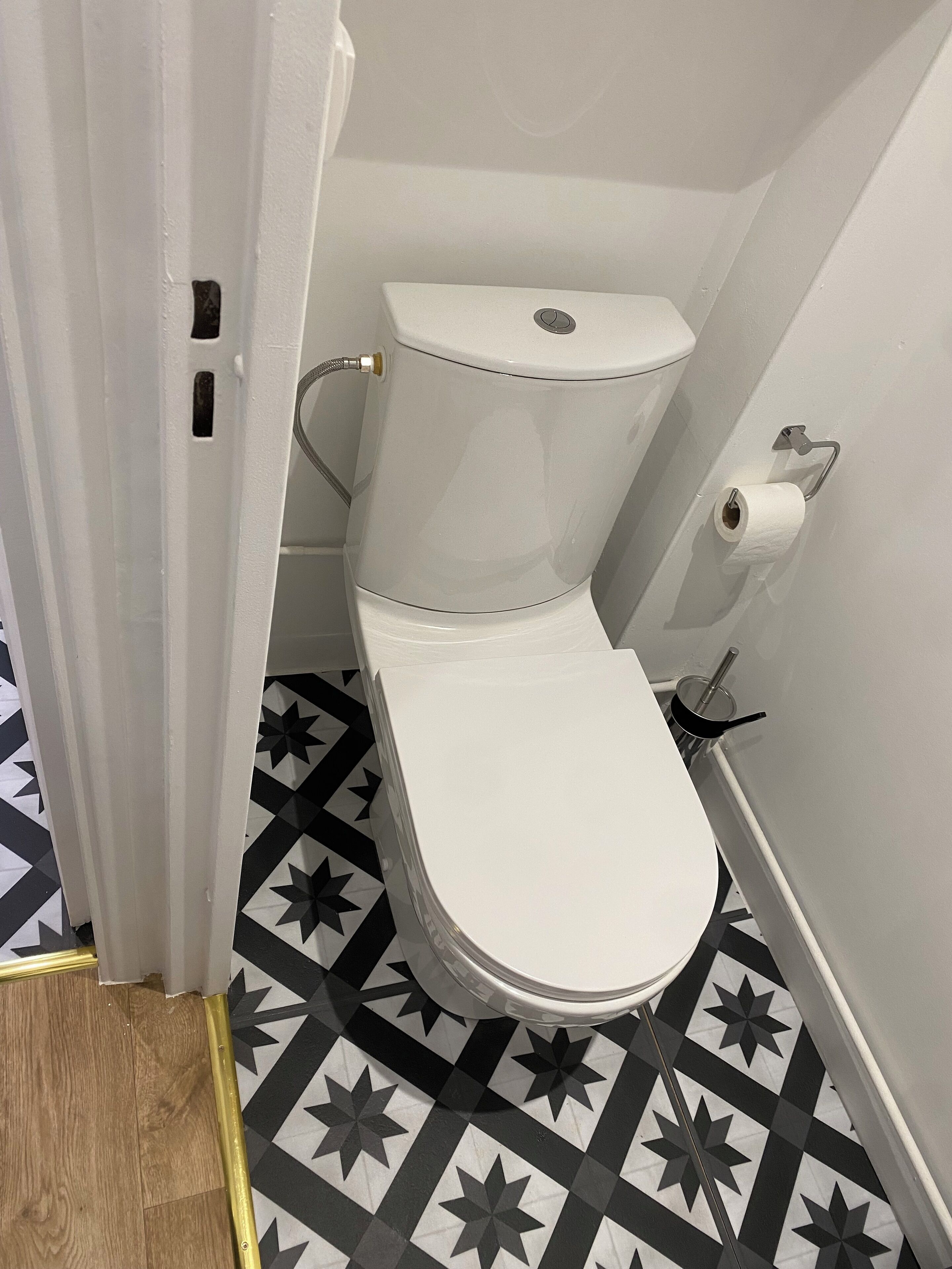 Een toilet met een witte tank en deksel, een toiletrolhouder en een vloer met een patroon.