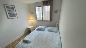 A bedroom with a bed, a nightstand, a lamp, a window with curtains, and a wall clock. - Pleasant apartment in the heart of the city (Orléans)