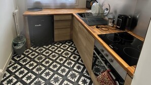 A compact kitchen with a black and white star-patterned floor, wooden cabinets, a black stove, and a window with a city view. - Pleasant apartment in the heart of the city (Orléans)