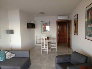 A living room with a sofa, a dining table with chairs, a TV, and a poster on the wall. - Apartment 'Mijas' with Sea View, Wi-Fi and Air Conditioning (Málaga)