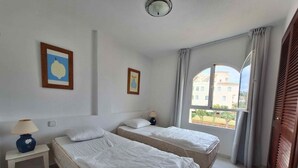 Ett hotellrum med två sängar, ett litet bord med en lampa och ett fönster med utsikt över byggnader.