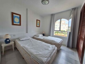 Une chambre d’hôtel avec deux lits, une petite table avec une lampe et une fenêtre donnant sur des immeubles.