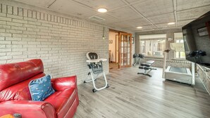 Une pièce avec un mur en briques, un canapé en cuir rouge, un transat pour bébé, un tapis de course et un téléviseur.