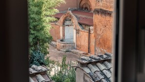 Une vue à travers une fenêtre donnant sur une cour intérieure avec une fontaine, des toits couverts de tuiles et un bâtiment à la façade rouge.