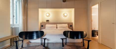 A bedroom with a bed, two chairs, a window, and a door.