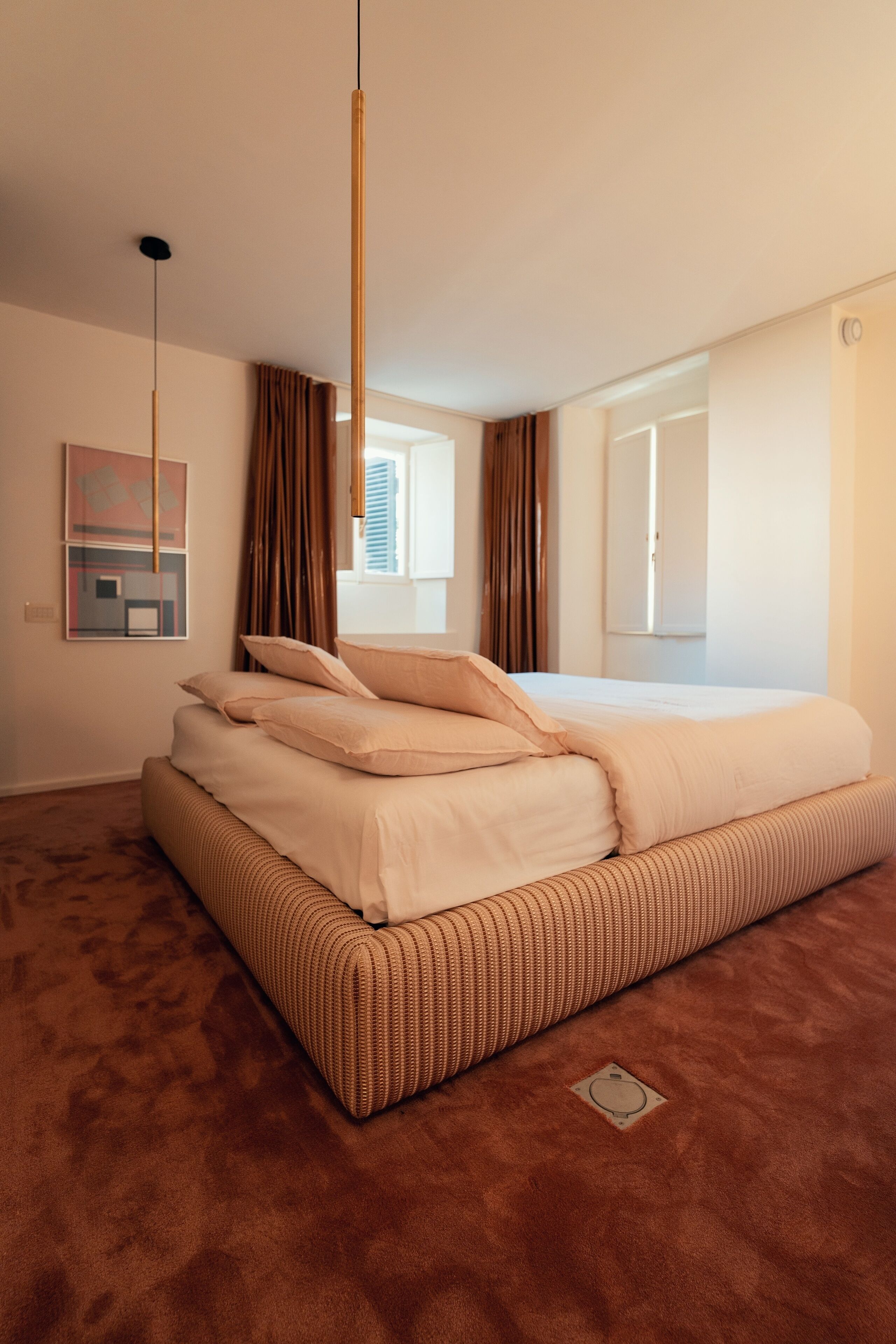 Un dormitorio con una cama grande, una lámpara colgante, una ventana con cortinas y una puerta que da a otra habitación.