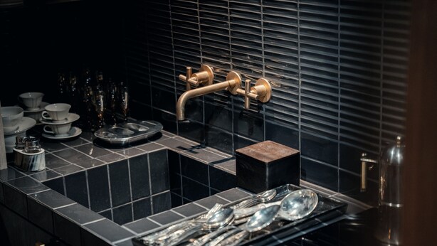 Une cuisine moderne avec des carreaux noirs, un évier doté d’un robinet doré et des ustensiles rangés avec soin.
