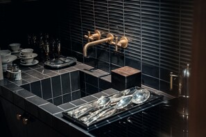Una cucina moderna con piastrelle nere, un lavello con rubinetto dorato e utensili disposti con ordine.
