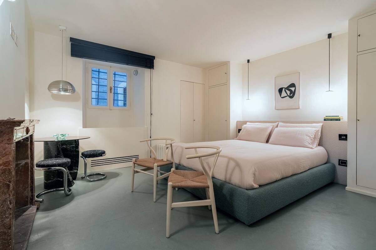 Une chambre à coucher avec un lit, deux chaises, une petite table et une fenêtre.