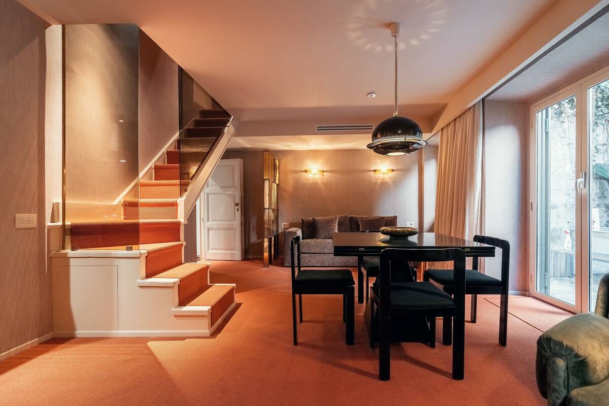Un intérieur moderne avec un escalier, un coin repas et de grandes fenêtres.