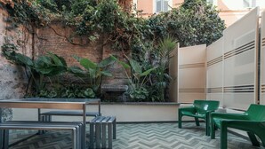 Un espace patio doté d’un sol en motifs de chevrons, d’une table en métal avec des bancs et de chaises en plastique vertes.