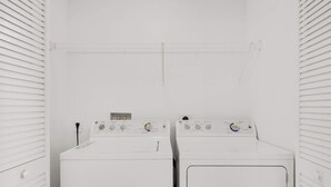 A laundry room with two front-loading washing machines and a dryer. - Large 2-Bedroom Condo Near Ocean w Amenities 1009 (Hallandale Beach)