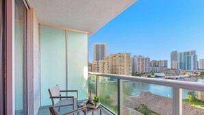 A balcony with a view of a city skyline, a table with a bottle and grapes, and a chair. - Large 2-Bedroom Condo Near Ocean w Amenities 1009 (Hallandale Beach)