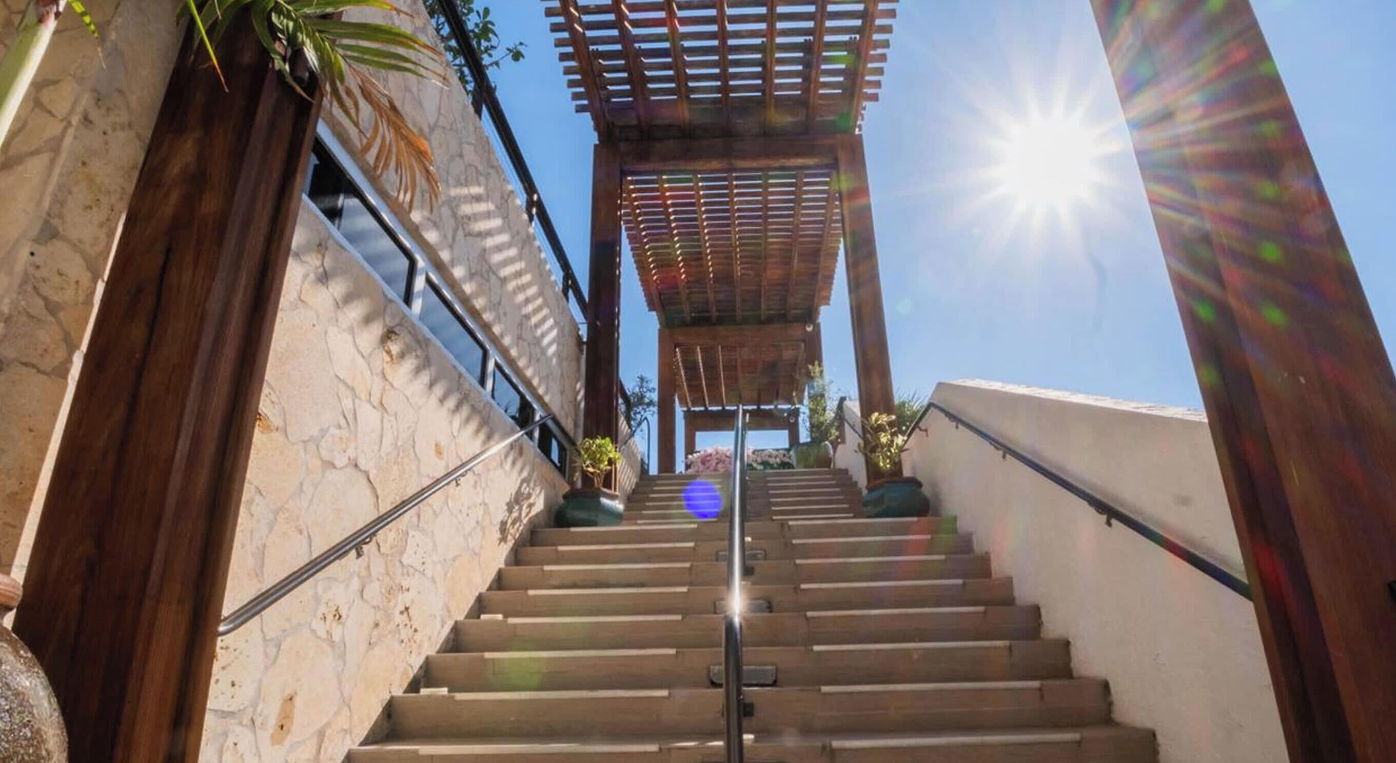 A staircase leading to a covered area with a pergola, surrounded by stone walls and potted plants.