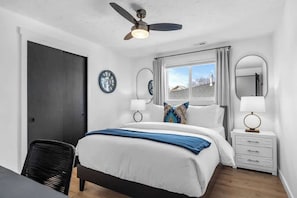 A bedroom with a bed, bedside tables, a ceiling fan, a window, and a door. - Spokane Apartment - North Atlantic Suite (Spokane)
