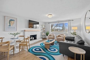 A modern living room with a fireplace, a dining area with wooden chairs, a sofa, and a coffee table. - Spokane Apartment - North Atlantic Suite (Spokane)